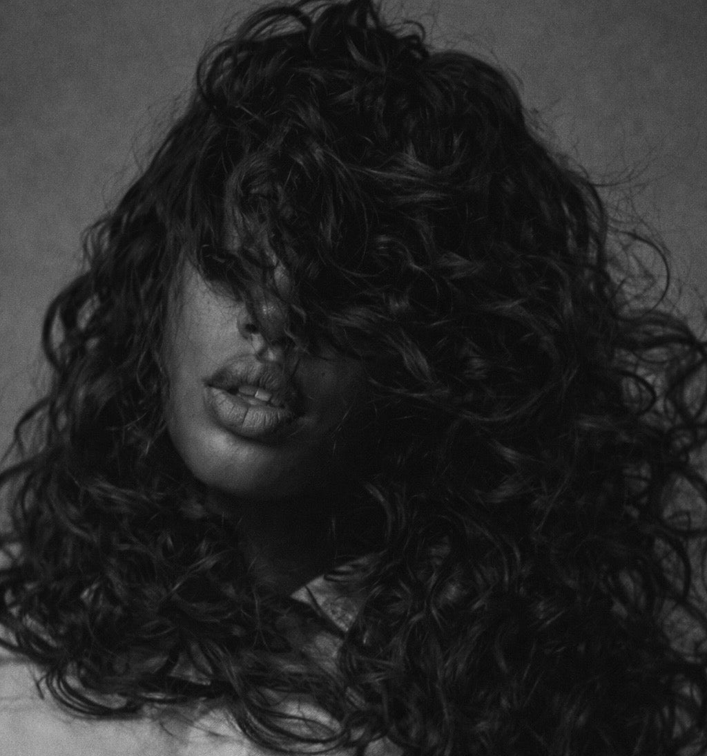 Person with long, curly hair covering their face against a dark background. Raw Curly Hair. Curly Bundle