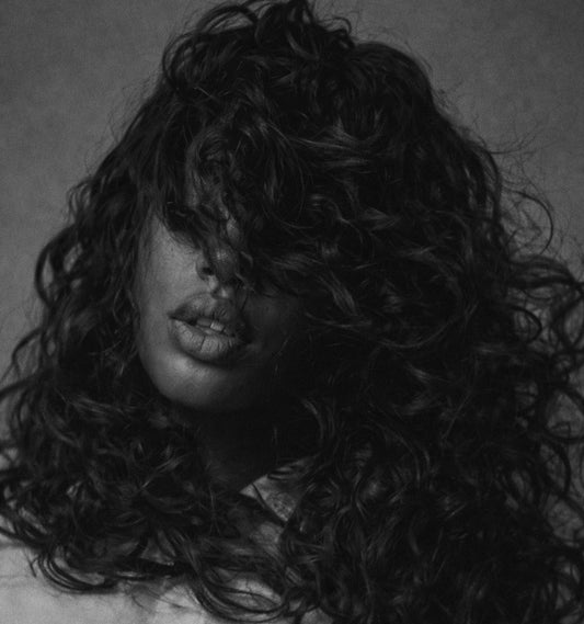 Person with long, curly hair covering their face against a dark background. Raw Curly Hair. Curly Bundle