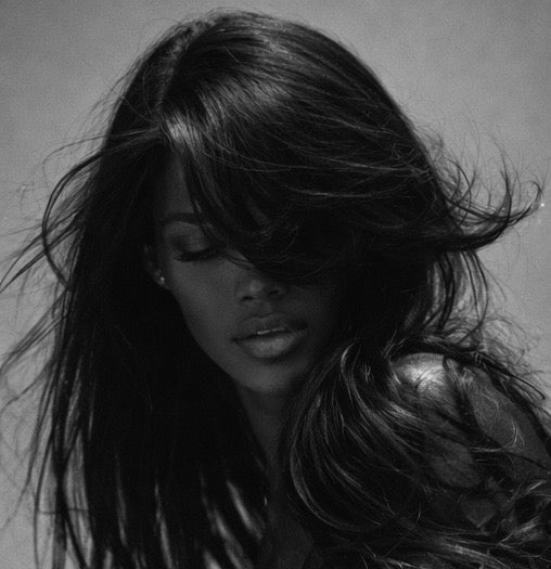 Black and white portrait of a woman with long hair, wearing a shiny outfit.